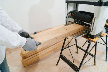hands of carpenter in protective gloves for working with wood on planing machine