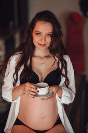 a beautiful pregnant woman with a naked tummy drinks coffee.の写真素材