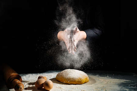 women kneads dough and scatters flour on a black background.の写真素材