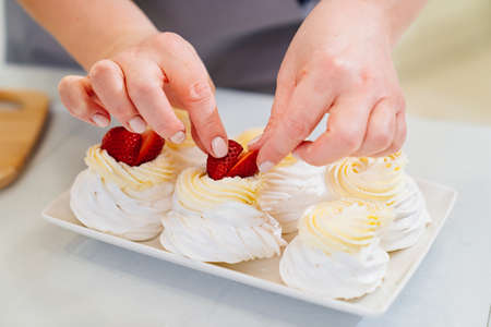 woman cook decorates cakes anna pavlova with strawberries and blueberriesの写真素材