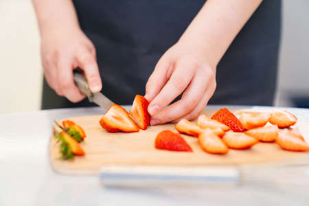 strawberries are cut into pieces on a wooden cutting board to decorate desserts.