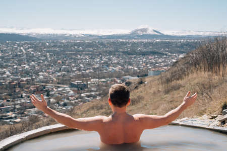 view from back. a man bathes in a hydrogen sulfide thermal spring.の写真素材