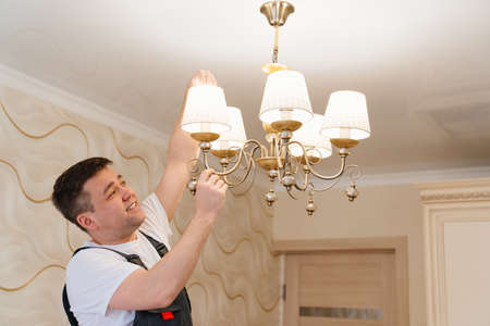 A male electrician changes the light bulbs in the ceiling light.の写真素材