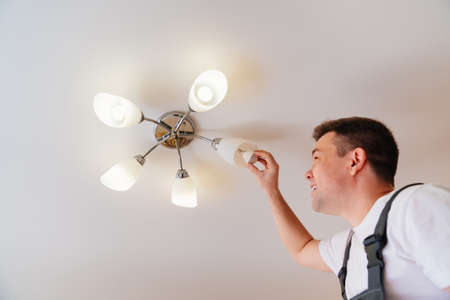 A male electrician changes the light bulbs in the ceiling light.