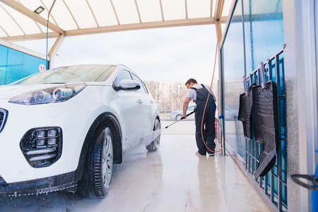 self-service car wash. a man in a work jumpsuit washes the car from a hose.の写真素材