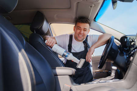 self-service car wash. man in work jumpsuit vacuuming car cabin after washingの写真素材