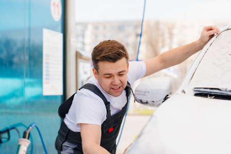 self-service car wash. a man in a work jumpsuit washes the car with a spongeの写真素材