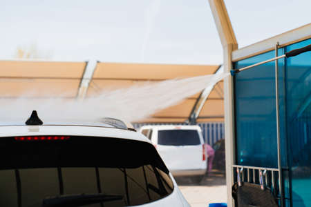 self-service car wash. a person washes the car from a hose.