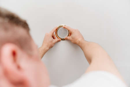 A male electrician changes the light bulbs in the spotlight ceiling lampの写真素材