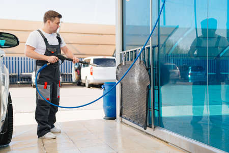 self-service car wash. a man in a work jumpsuit washes the car mat from a hose.