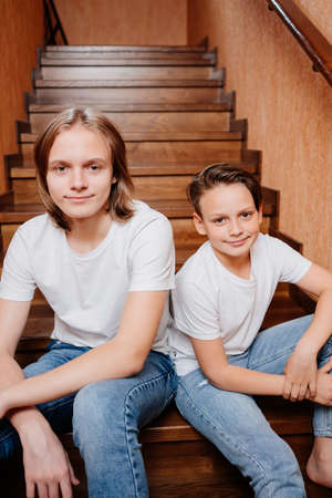 two brothers of a teenager in white T-shirts and jeans on a wooden staircaseの写真素材