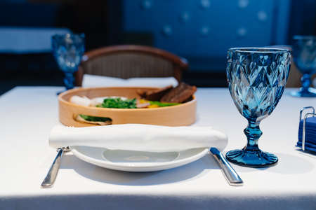 white plate with napkin and cutlery, beautiful blue glass wine glass on table.