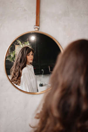 a beautiful woman in a white shirt looks at her reflection in a round mirror.の写真素材