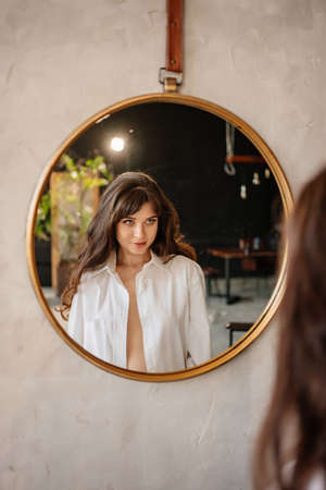 a beautiful woman in a white shirt looks at her reflection in a round mirror.の写真素材