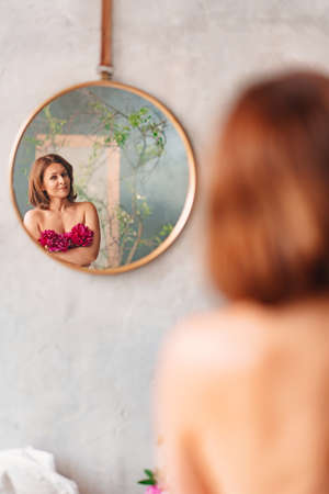 an attractive woman with a bouquet of peonies looks at her reflection topless.の写真素材