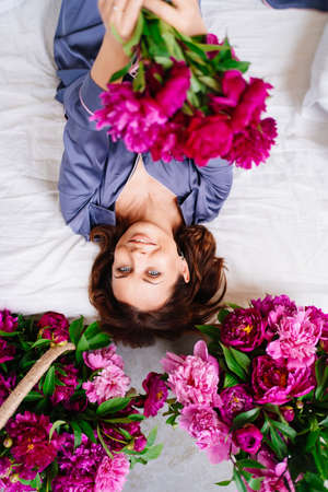 happy morning. a woman in pajamas in bed with a peonies.の写真素材