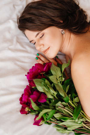 a gentle brunette woman in bed with a bouquet of peonies. morning of holiday.の写真素材