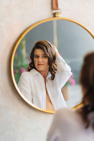 a brunette woman in a white shirt looks at her reflection in a round mirror.の写真素材