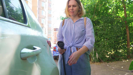 woman plugging in an electric car at outlet socket.