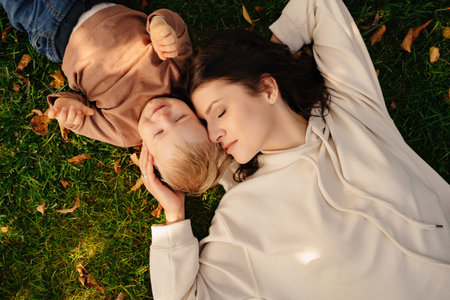 an attractive woman with a little son lies on a green lawn with autumn leaves.の写真素材