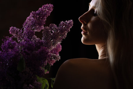 profile of a beautiful blonde woman with a bare shoulder and a bouquet of lilacsの写真素材