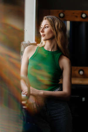 a young attractive blonde woman in a green top by the window. solar flare