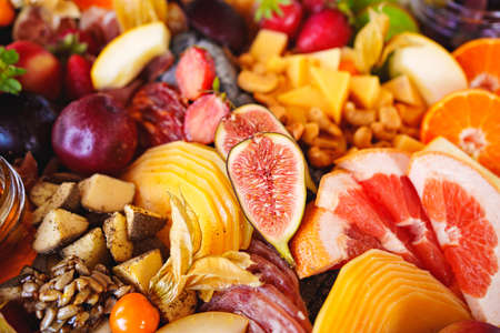 assorted fruits, berries, cheese, sausage, snacks and honey on a tray.