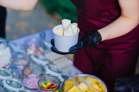 Gloved hands make roll ice cream and put in a paper cup for an outdoor party.
