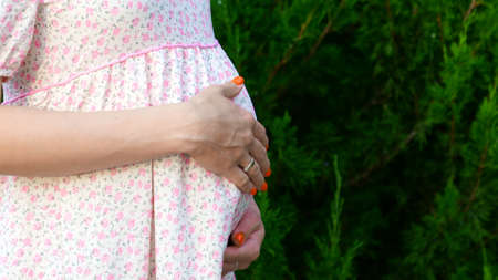 a pregnant woman in a summer dress strokes her stomach.の写真素材