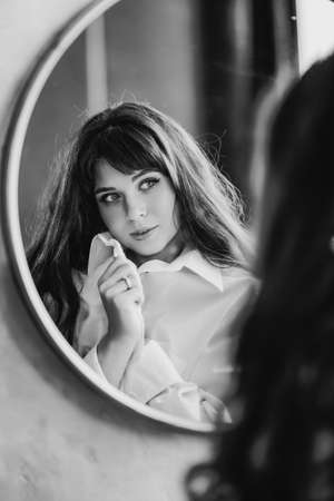 a woman in a white shirt looks at reflection in a round mirror. black and whiteの写真素材