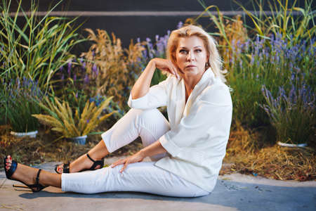 woman in white pantsuit on the floor in dark room with lavenderの写真素材