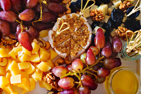 assorted fruits, berries, cheese, snacks and honey on a tray.の写真素材