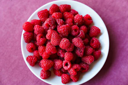 a white plate with raspberries on the table.の写真素材