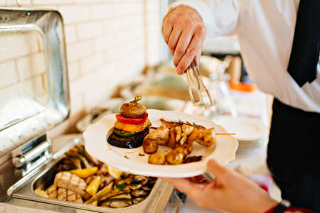 the waiter puts fried fish and vegetables from Chafing Dish on a plate.の写真素材