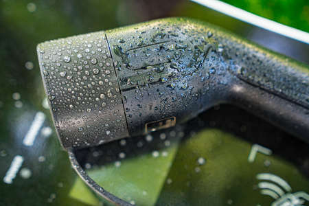 a electric car charger with water droplets. reflection of urban greenery.