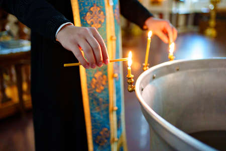 priest lights candles on the font for baptism in Orthodox Church.