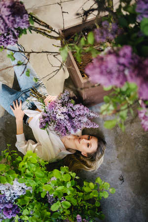 view top. a blonde in a white shirt and jeans on the floor with lilac flowers.の写真素材
