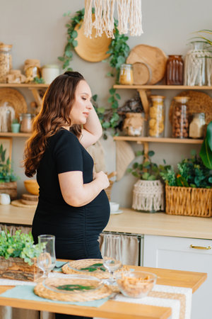 a pregnant woman in a black dress in the kitchen of the house.の写真素材