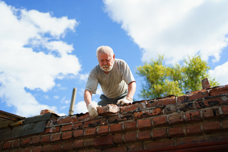 an elderly man dismantles the old brickwork and lays new bricks on the roof.の写真素材