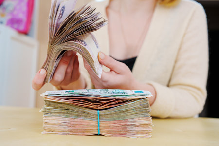 womens hands hold a stack of rubles tied with a rubber band.