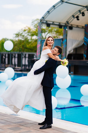 bride and groom in classic clothes by the pool decorated with white balloons.の写真素材