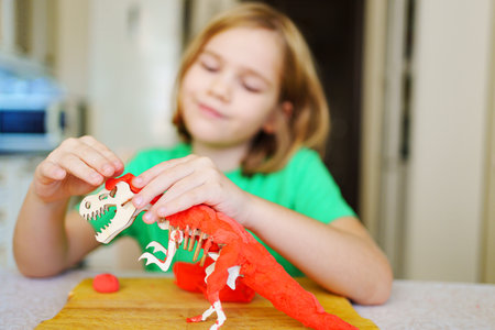 A blonde little girl makes a dinosaur craft out of wood and air plasticine.