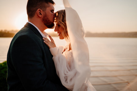 the bride and groom under the veil on the sunset by the riverの写真素材