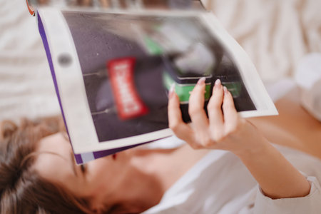 an attractive and happy woman lies in bed and reads a magazine.の写真素材