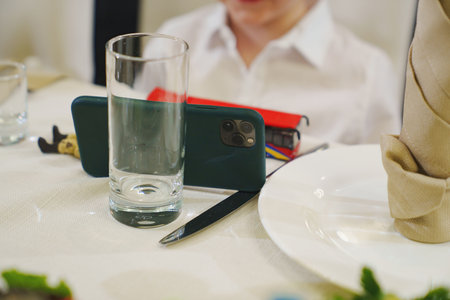 The boy put the smartphone on the table using a glass and a knife as a stand.の写真素材
