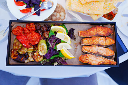 rectangular black dish with grilled fish and vegetables.の写真素材