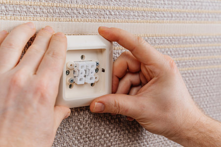 male hand replaces or repairs the light switch on the wall with brown wallpaper.の写真素材