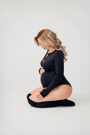 a beautiful and calm pregnant blonde in a black bodysuit in a white room.の写真素材