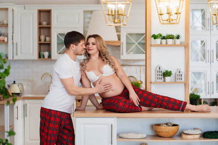 a pregnant woman and a man in pajamas flirt in the kitchenの写真素材