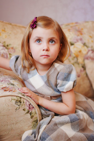 a portrait of a cute sad little girl in a plaid dress on the couch.の写真素材